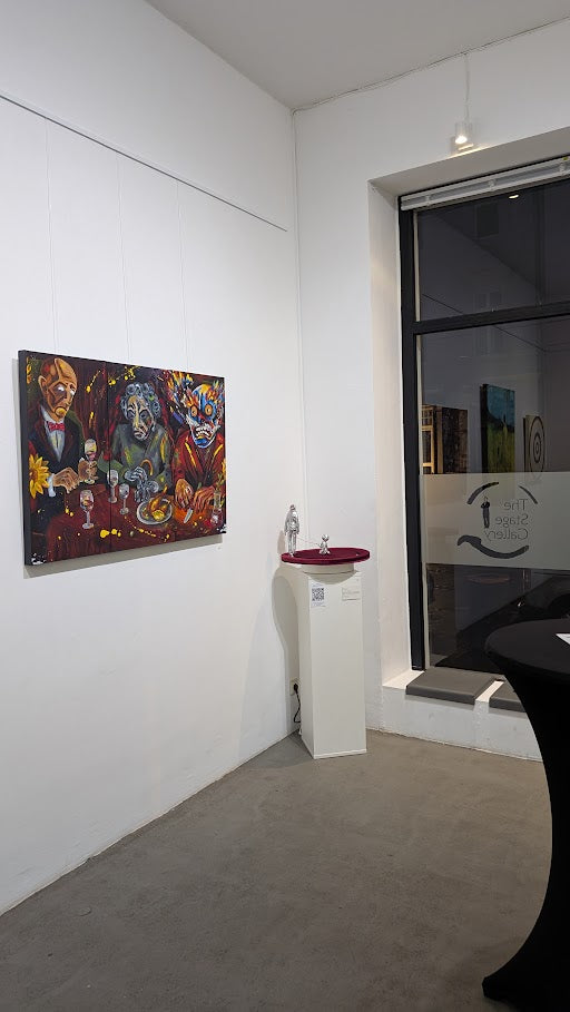 Ausstellungsansicht mit dem Werk „Dinner for (every)one – ein Anti-Abendmahl“ von Jasmin Meirose, 2025. Das farbintensive Triptychon hängt an einer weißen Galeriewand, beleuchtet, mit Blick Richtung Eingang und weiteren Arbeiten im Hintergrund.